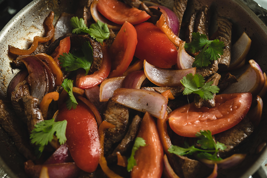 Lomo Saltado peruano listo en el wok con tomate, cebolla, cilantro y salsa de soya