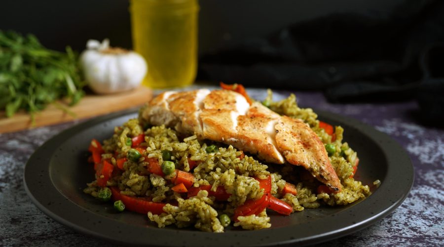 Plato de Arroz con Pollo peruano con pollo dorado sobre arroz verde servido en plato negro sobre mesa oscura - Plate of Peruvian arroz con pollo with golden chicken over bright green cilantro rice served on a dark plate