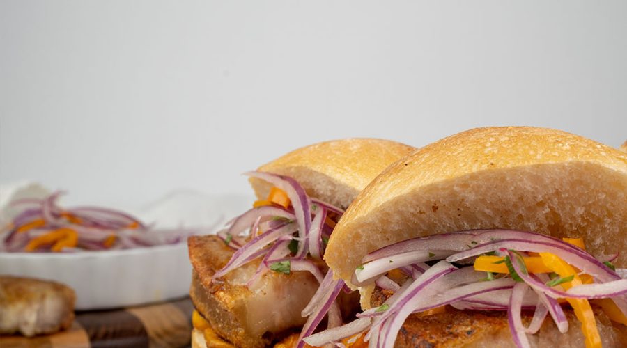 Peruvian pan con chicharrón with pork belly, sweet potato, and salsa criolla