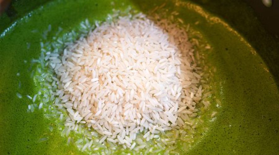 Arroz crudo siendo agregado sobre la base verde de cilantro y ají amarillo en una olla - Raw rice being added to the green cilantro and ají amarillo base in the pot for Peruvian arroz con pollo