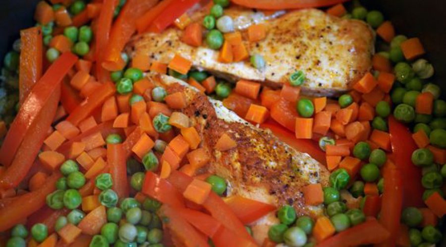 Piezas de pollo dorado cocinándose encima de vegetales coloridos, zanahorias, arvejas y pimientos rojos, en la olla durante la preparación - Golden chicken pieces resting on top of colorful vegetables, carrots, peas, and red peppers, cooking in the pot during the arroz con pollo preparation